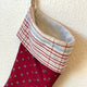 Red Christmas stocking with plaid trim hanging on a textured white wall.