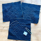 Three pieces of blue fabric with white embroidery on a wooden surface, accompanied by a pair of scissors.