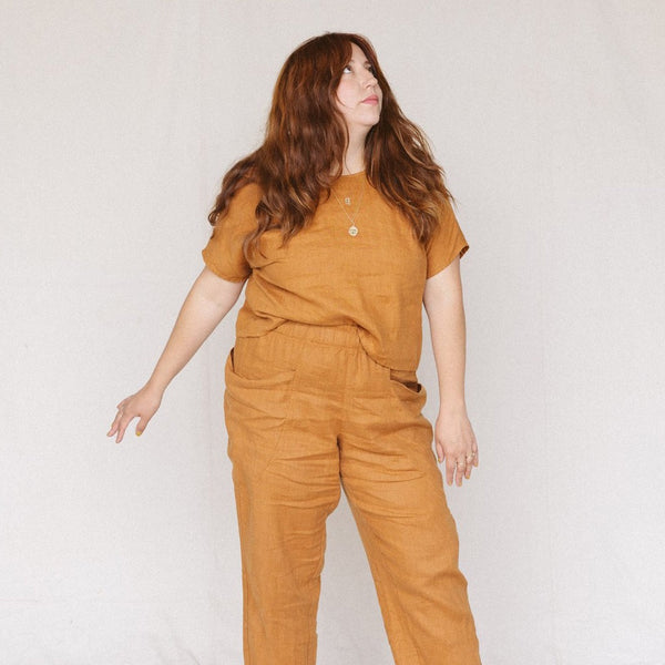 woman wearing rust colored crop top and matching linen pants, her arm is out and she is looking up