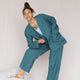 woman wearing teal linen jacket and teal linen pants leaning her right arm on her bent leg