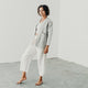 woman standing in a white room wearing white wrap pants and a light denim artist jacket