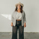 woman looking at camera standing in a white room wearing the denim artist jacket and a white top