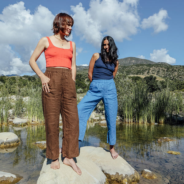 Two women standing on rocks by a body of water with a scenic background