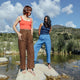 Two women standing on rocks by a body of water with a scenic background