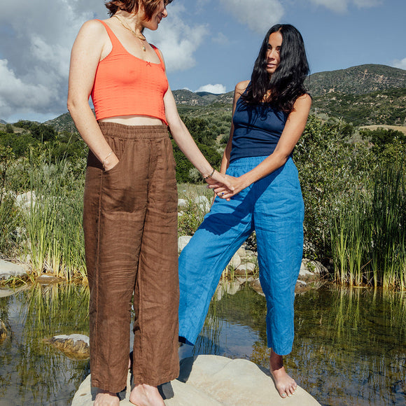 Two women standing on rocks by a lake with mountains in the background