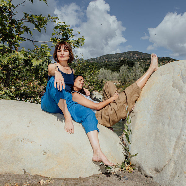 Two people sitting on large rocks with a scenic background of trees and mountains.