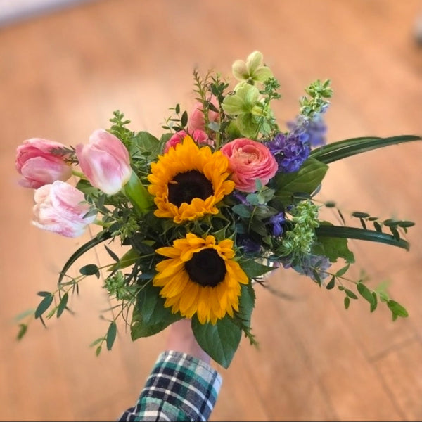 Bouquet of flowers with sunflowers and pink tulips held by a person on a wooden surface.