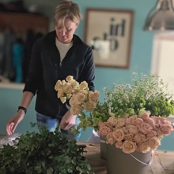 Person arranging flowers in a room with a blue wall and framed picture.