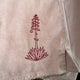 A close-up of a light beige or off-white fabric garment, likely shorts or a shirt, featuring a dark red embroidered illustration of a succulent plant on the leg.