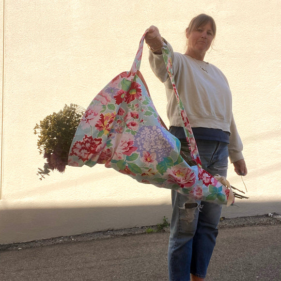 Person holding a large floral bag outdoors with a plain background