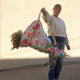 Person holding a large floral bag outdoors with a plain background