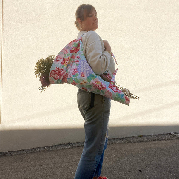 Person holding a large floral-patterned bag against a plain background