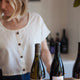 cropped image of a woman in a wine shop with wine bottles in front of her wearing a natural hemp crop top with buttons on the front