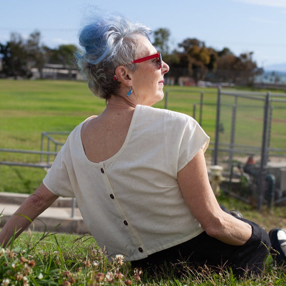 image of the back of a woman sitting on grass wearing a cream hemp crop top with buttons on the back