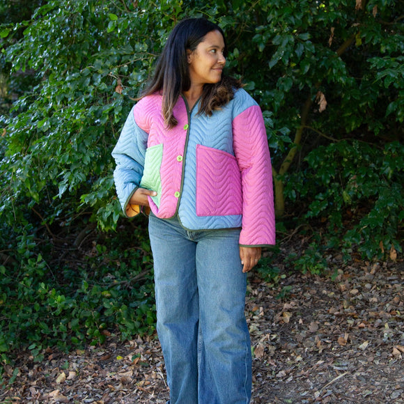 image of a woman wearing a multi colored cropped quilted coat in front of green bushes