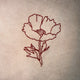 A close-up of a beige woven textile, likely a table runner or napkin, featuring a simple embroidered poppy flower in dark red thread.