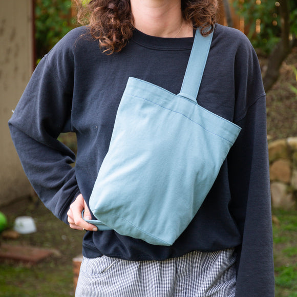 Person wearing a light blue tote bag over one shoulder outdoors.