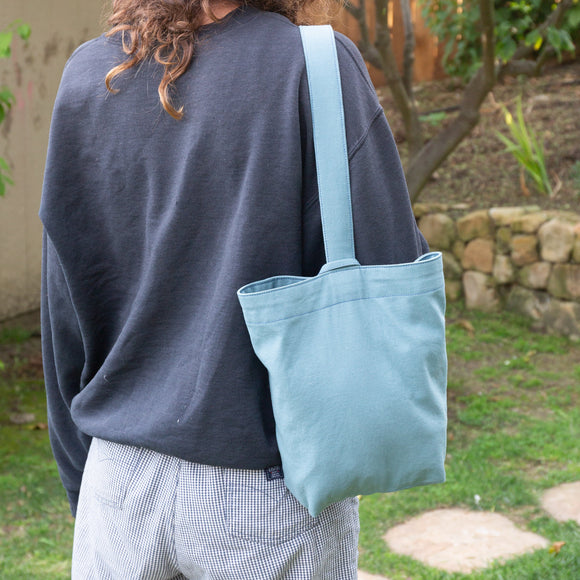 Person wearing a gray shirt and light blue tote bag outdoors