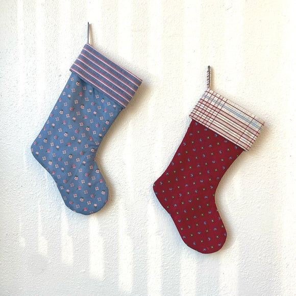 Two patterned Christmas stockings hanging on a white curtain.
