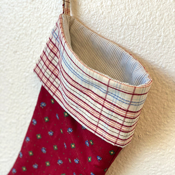 Red Christmas stocking with plaid trim hanging on a textured white wall.