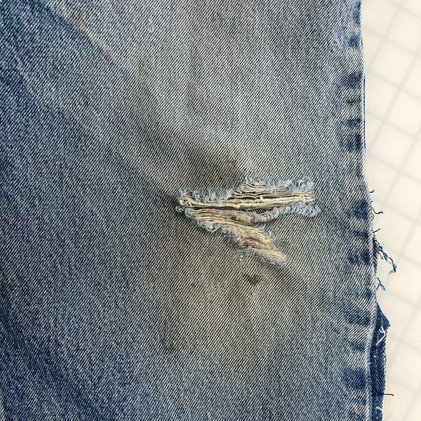 Close-up of a blue denim fabric with a tear and frayed edge.