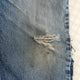 Close-up of a blue denim fabric with a tear and frayed edge.