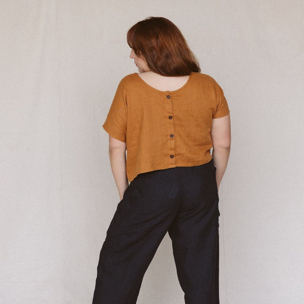 back view of a woman wearing a rust colored crop top with buttons in the back and she is looking to the side