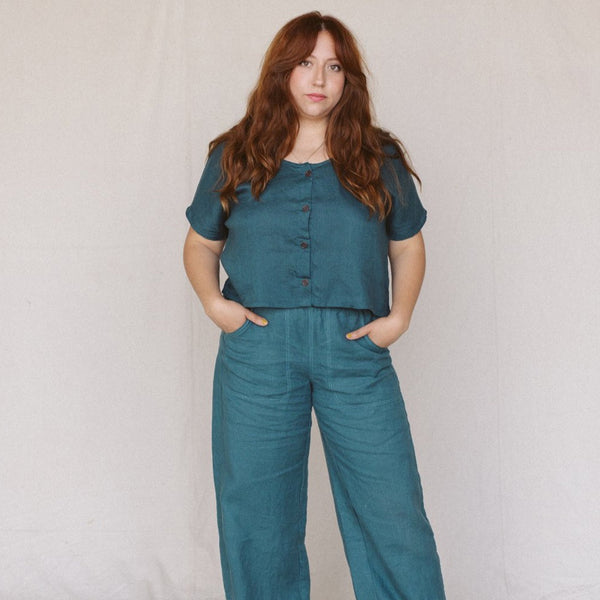 front view of woman wearing teal linen crop top with buttons in front and matching teal linen easy sailor pants with her hands in the pockets