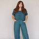 front view of woman wearing teal linen crop top with buttons in front and matching teal linen easy sailor pants with her hands in the pockets