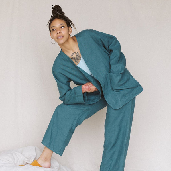 woman wearing teal linen jacket and teal linen pants leaning her right arm on her bent leg