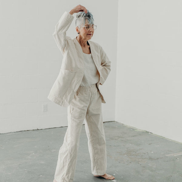 Woman in motion with her hand above her head wearing cream canvas jacket and matching pants