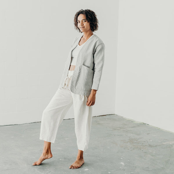 woman standing in a white room wearing white wrap pants and a light denim artist jacket