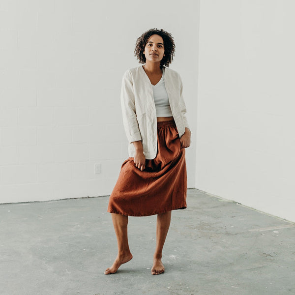 woman wearing a rust colored linen skirt with cream colored canvas artist jacket looking at camera
