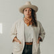 woman looking at camera wearing a cowboy hat and cream canvas jacket with hands in pockets